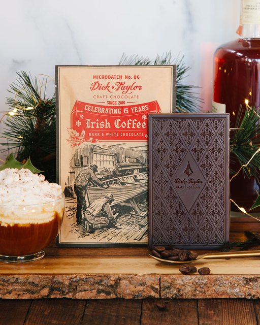 Irish coffee with a bottle of Dick Taylor craft chocolate and a vintage-style poster on a wooden surface.