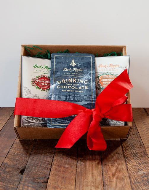 Box of winter favorites drinking chocolate, peppermint bark, orange bourbon pecan with red ribbon